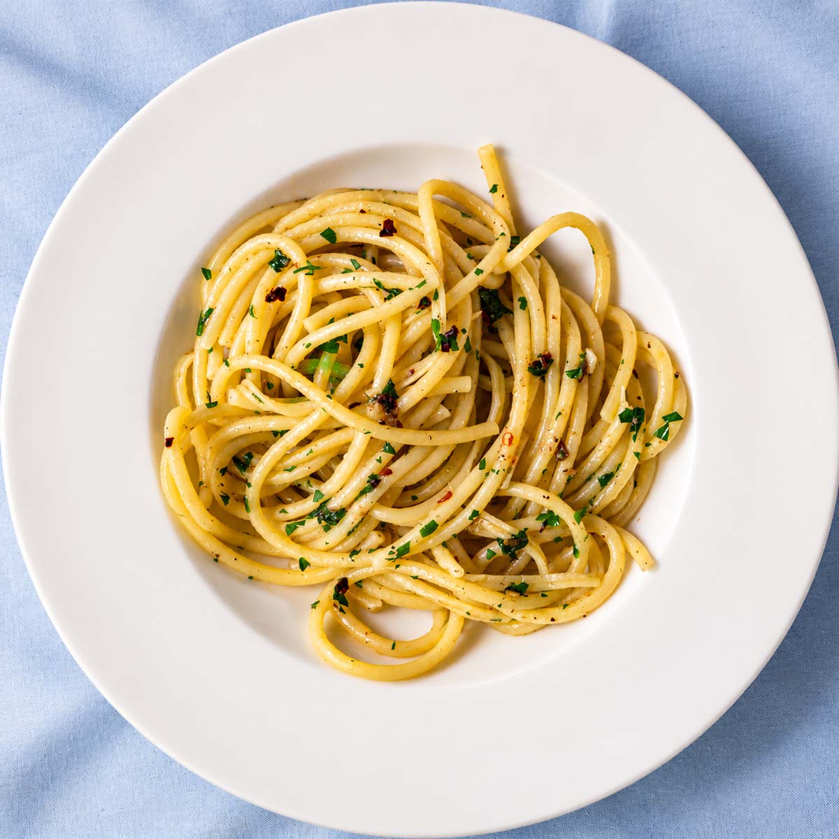 Anchovy pasta with spaghetti, parsley, red pepper flakes, and garlic on a white plate