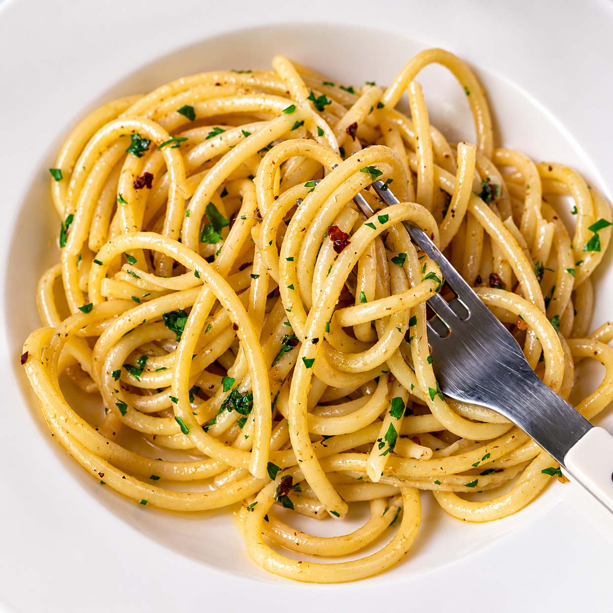 Anchovy pasta with spaghetti twirled around a fork, parsley, garlic, and red pepper flakes