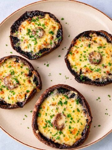 Baked portobello mushrooms topped with melted cheddar cheese and chopped parsley on a ceramic plate