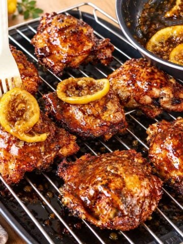 Glazed honey lemon chicken thighs on a wire rack with lemon slices and garlic sauce.
