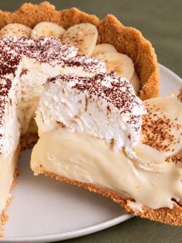 Banoffee pie with banana slices, creamy filling, whipped cream and chocolate dusting, with one slice lifted from the pie