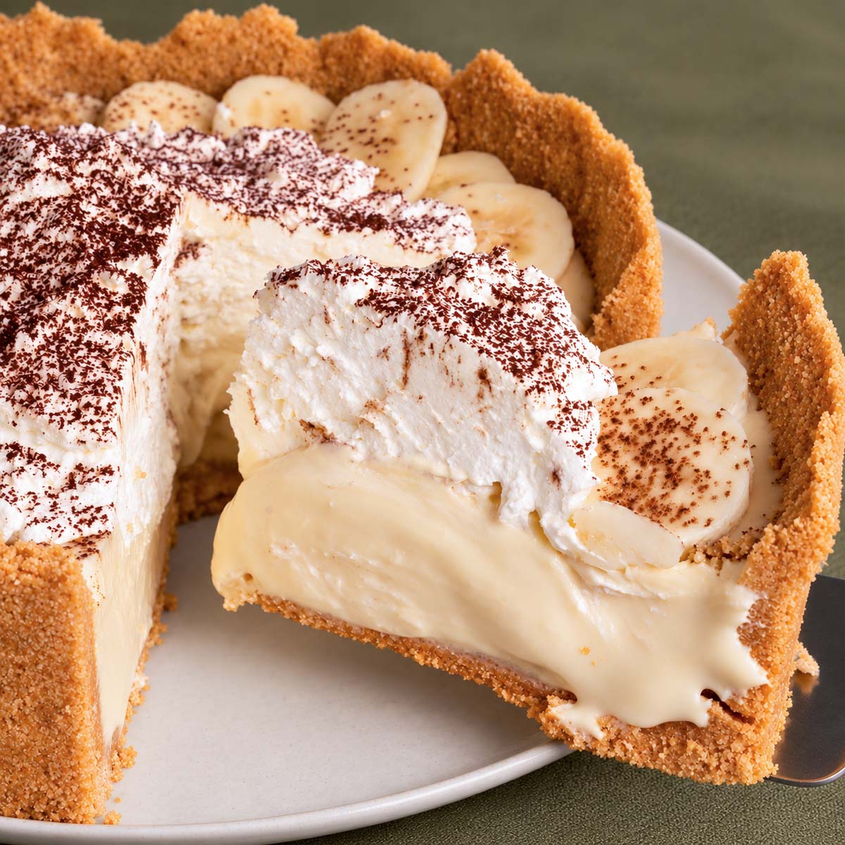 Banoffee pie with banana slices, creamy filling, whipped cream and chocolate dusting, with one slice lifted from the pie
