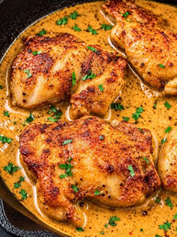 Boneless skinless chicken thighs seared until golden in a cast-iron skillet, simmering in a creamy pan sauce and topped with chopped parsley.