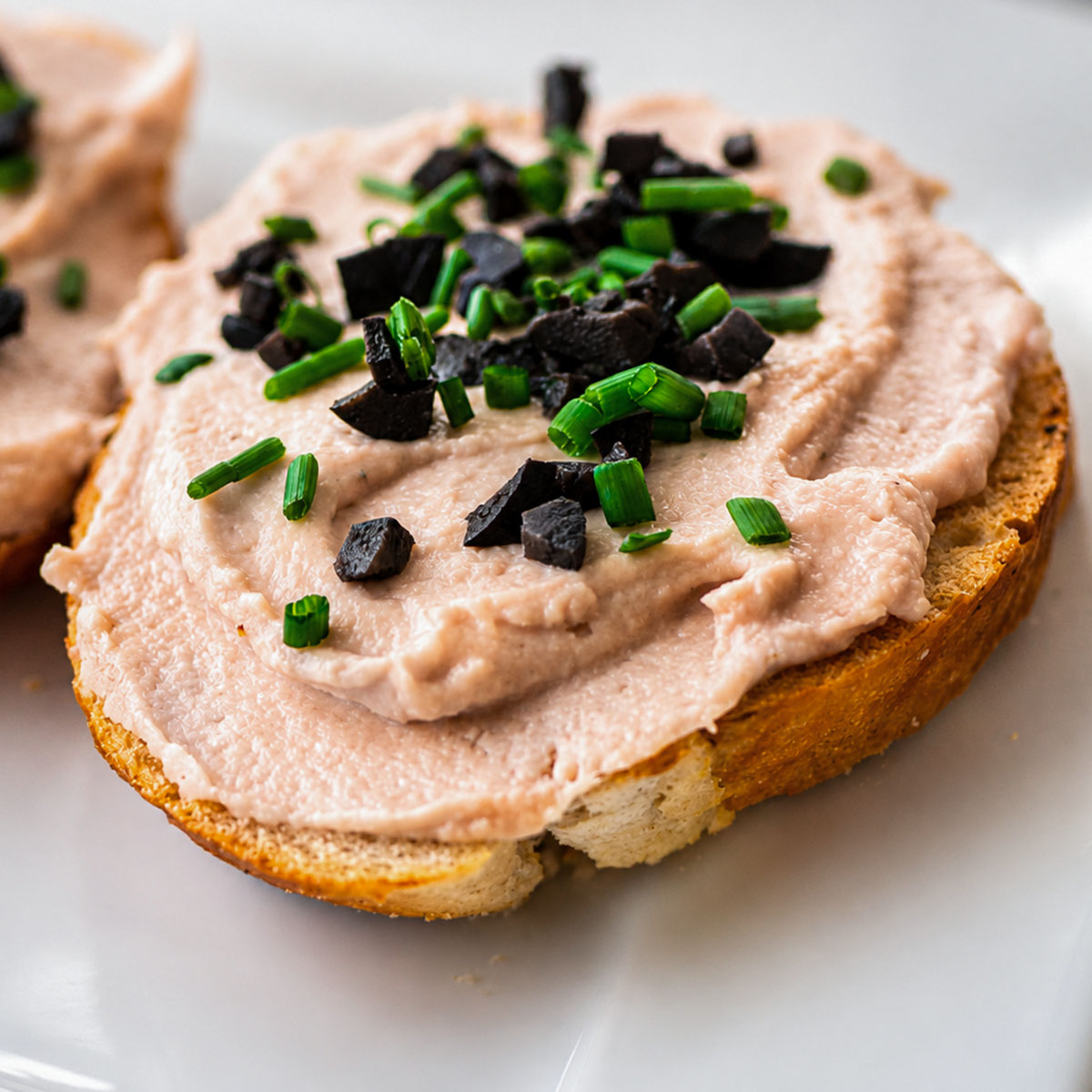 Close-up of creamy 3 ingredient tuna dip with cream cheese spread over toast and topped with black olives and chives.