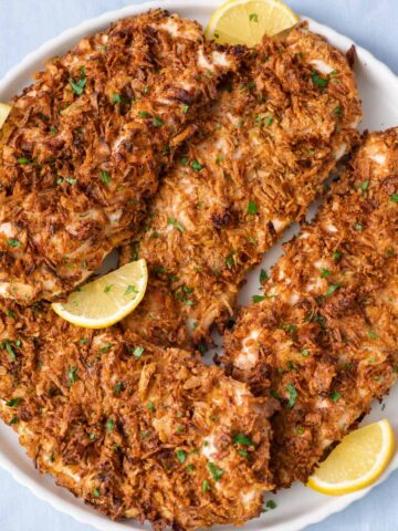 Crispy French onion chicken with a golden onion coating, garnished with parsley and lemon wedges on a white platter.