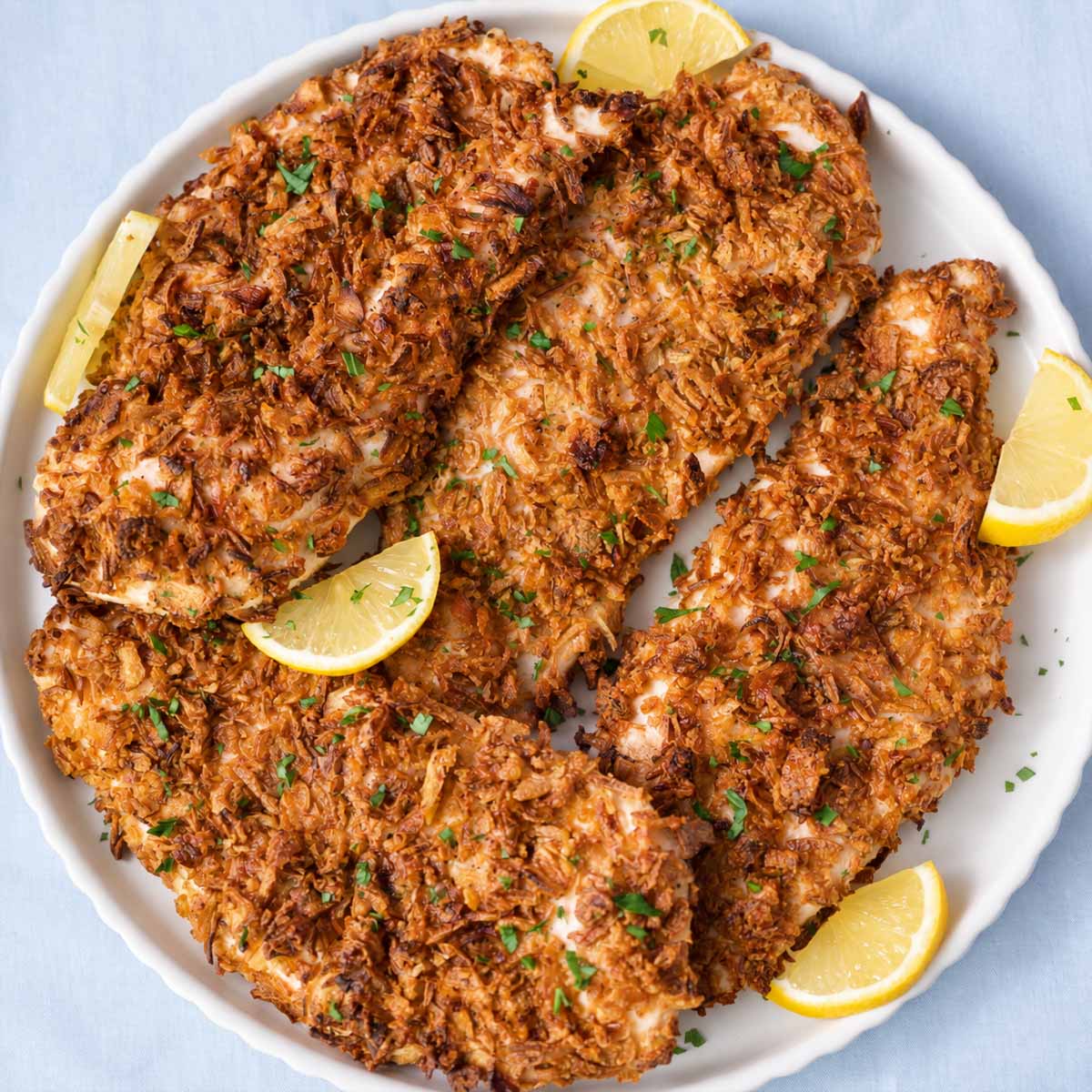 Crispy French onion chicken with a golden onion coating, garnished with parsley and lemon wedges on a white platter.