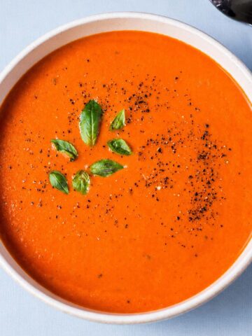 High protein tomato soup topped with fresh basil and black pepper in a ceramic bowl.
