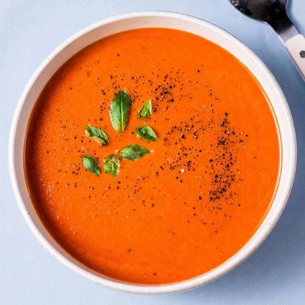 High protein tomato soup topped with fresh basil and black pepper in a ceramic bowl.