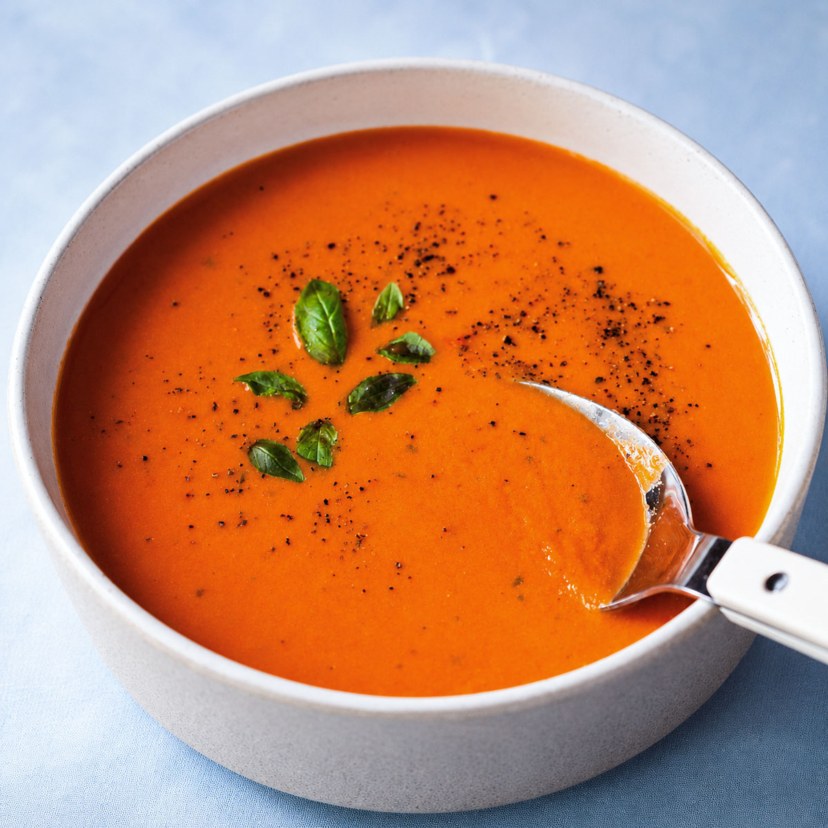 Creamy high protein tomato soup with basil and black pepper, served with a spoon.