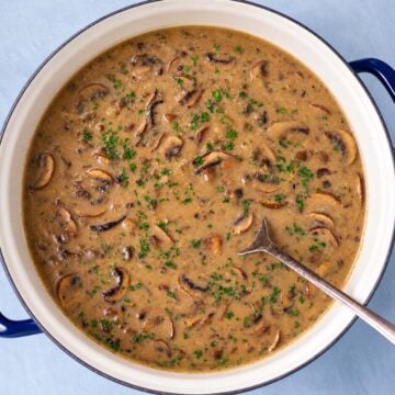 Mushroom soup without cream in a pot with sliced mushrooms and chopped parsley.