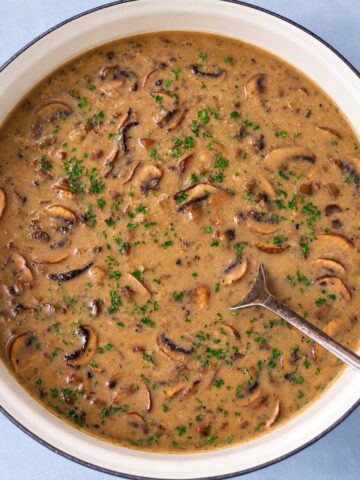 Mushroom soup without cream in a pot with sliced mushrooms and chopped parsley.