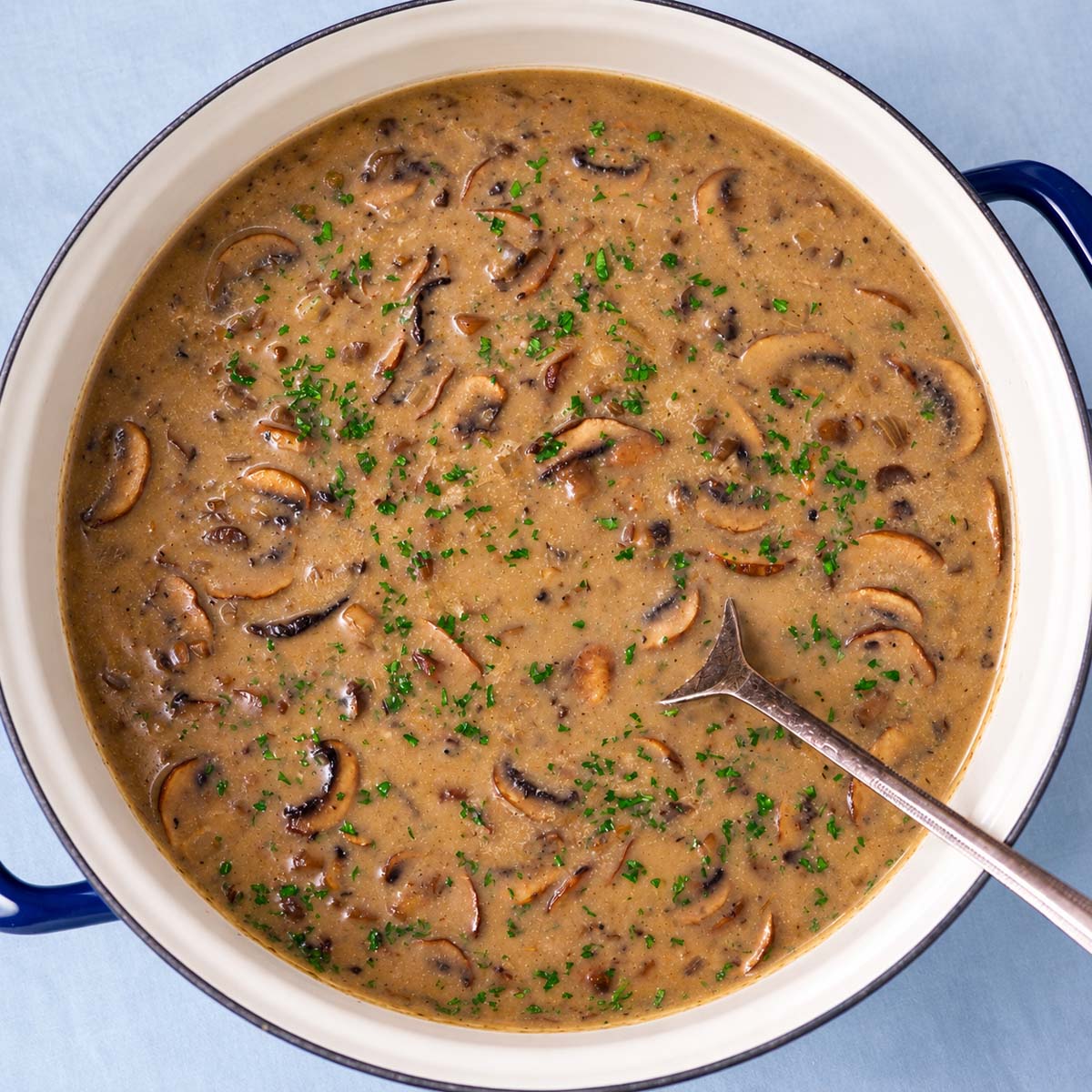 Mushroom soup without cream in a pot with sliced mushrooms and chopped parsley.