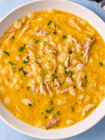 Pastina soup with shredded chicken and parsley in a white bowl