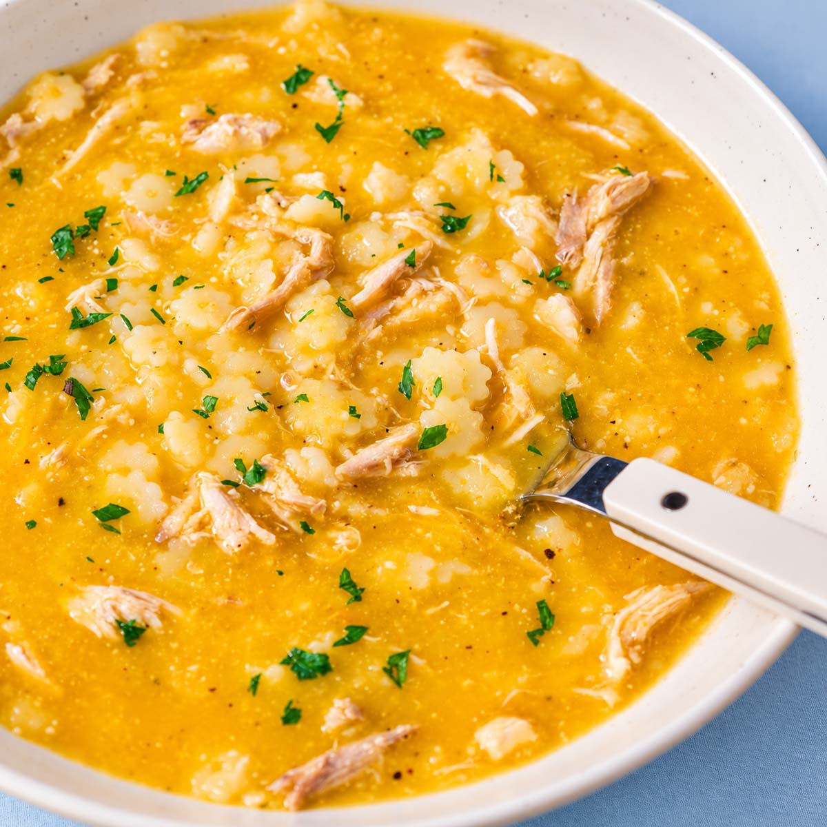 Bowl of creamy chicken pastina soup with a white-handled spoon