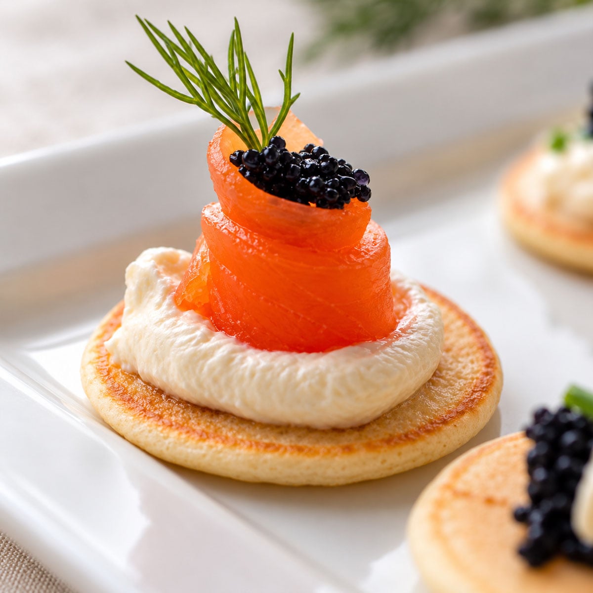 Close-up of a smoked salmon blini with crème fraîche, black fish roe, and fresh dill.