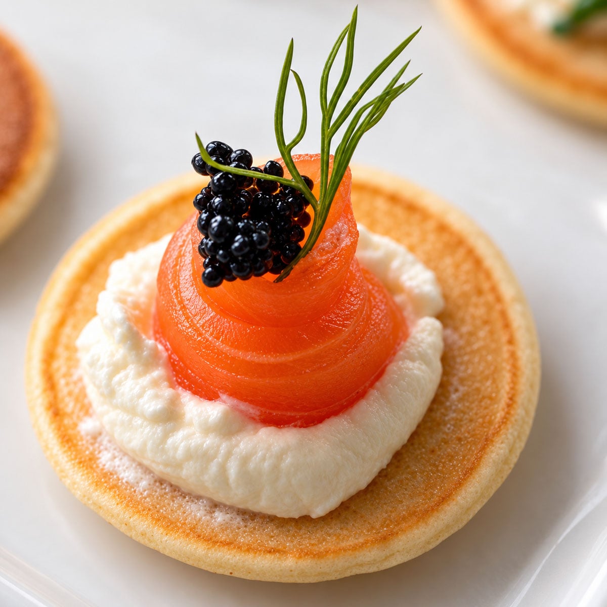 Top down Close-up of a smoked salmon blini with crème fraîche, black fish roe, and fresh dill.