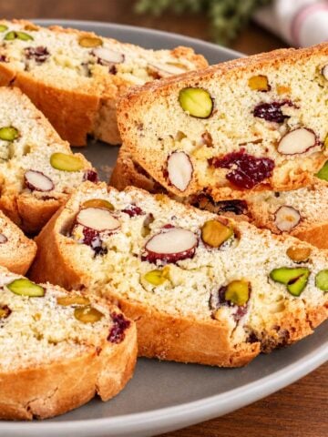 Almond pistachio cranberry biscotti slices on a plate, packed with nuts and dried cranberries, with one crisp biscotti.