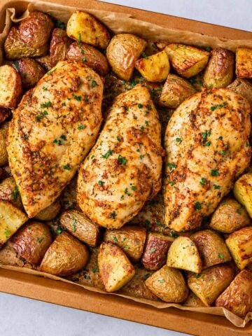 One pan chicken breast and potatoes roasted with garlic, herbs, and golden baby potatoes on a baking tray.