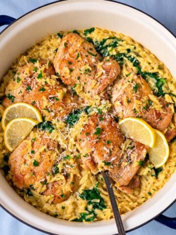One pot lemon chicken orzo with golden chicken thighs, creamy orzo, spinach, Parmesan, and lemon slices in a Dutch oven.
