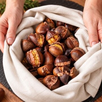 Roasted chestnuts wrapped in a beige linen cloth with cracked shells showing golden centers