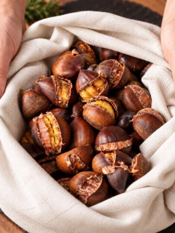 Roasted chestnuts wrapped in a beige linen cloth with cracked shells showing golden centers