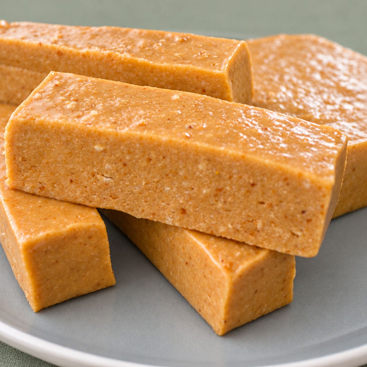 Stacked turrón de Jijona bars, showing their soft almond texture on a gray plate.